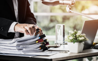 Businessman hands holding pen for working in Stacks of paper files searching information business report papers and piles of unfinished documents achieves on laptop computer desk in modern office